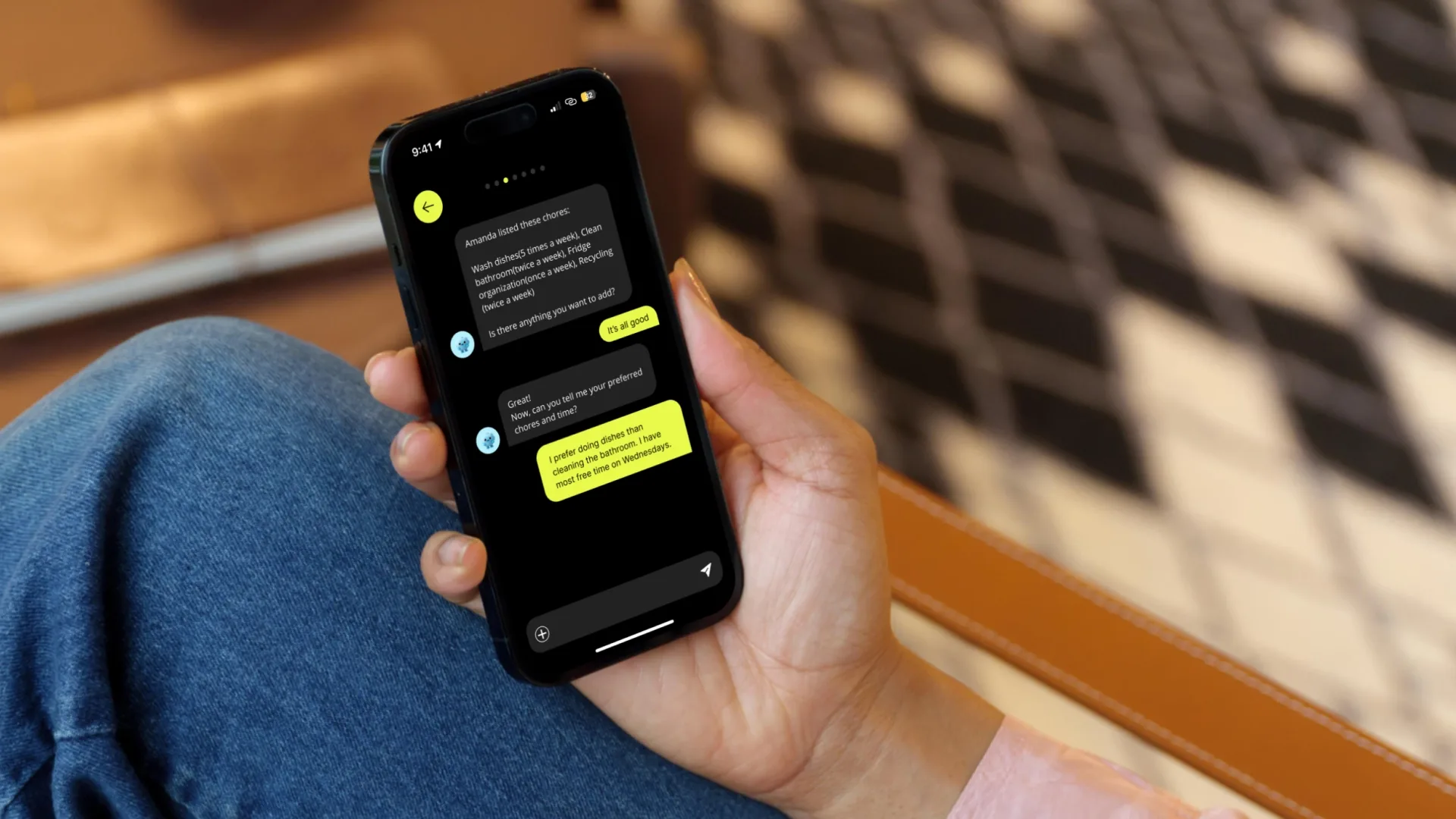 A hand holds a smartphone as a user chats during the app’s onboarding process, establishing their preferred household task schedules.
